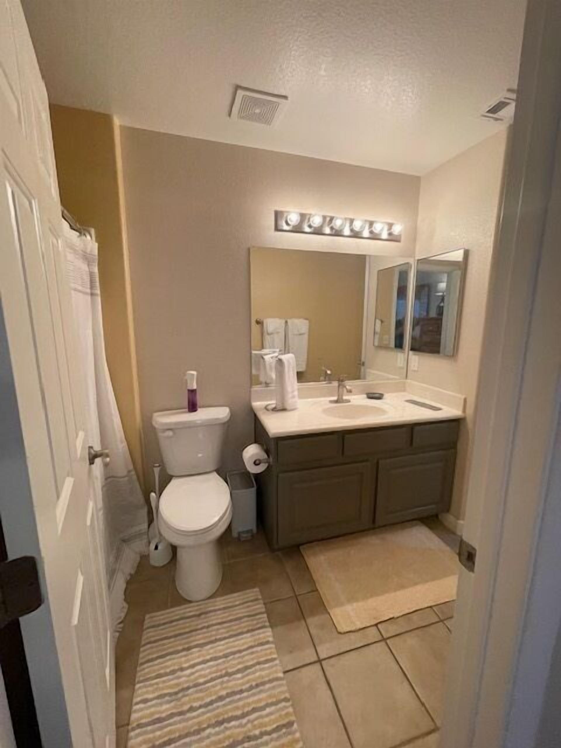A bathroom with a toilet, sink, mirror, and a light fixture above the mirror.