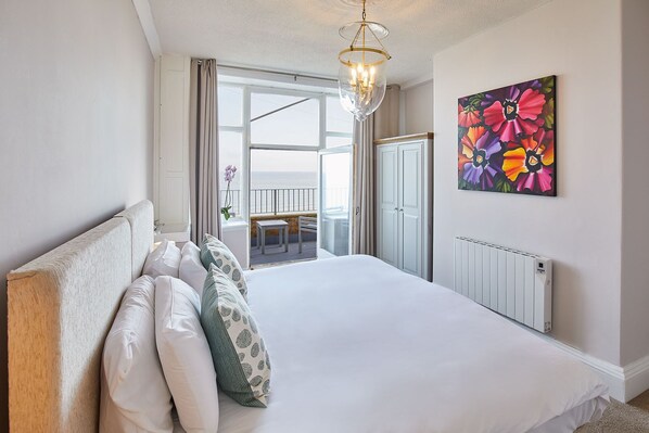 A bedroom with a large bed, a view to a balcony, a radiator, and a floral painting on the wall.