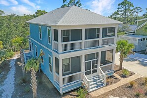 A two-story house with a balcony on the upper floor, surrounded by a landscaped garden with palm trees. - Get Outdoors at Song of the Sea~ WindMark Beach, Screened Deck, Perfect Location (WindMark Beach)