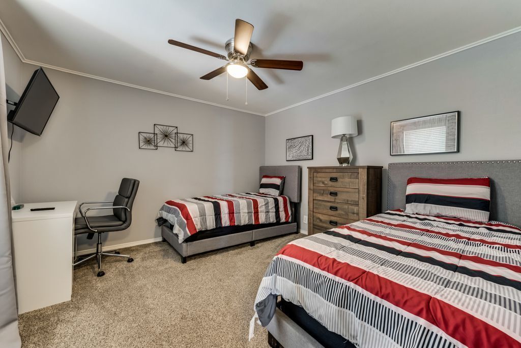 A bedroom with a bed, a desk, a chair, a dresser, and a ceiling fan.