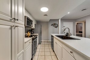 Una cocina moderna con armarios blancos, horno empotrado, microondas y lavamanos.
