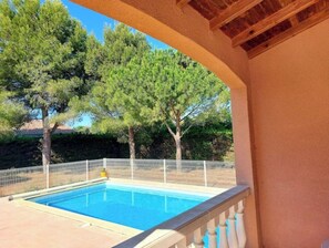 A swimming pool with a white fence, surrounded by trees and a covered area with a wooden ceiling.