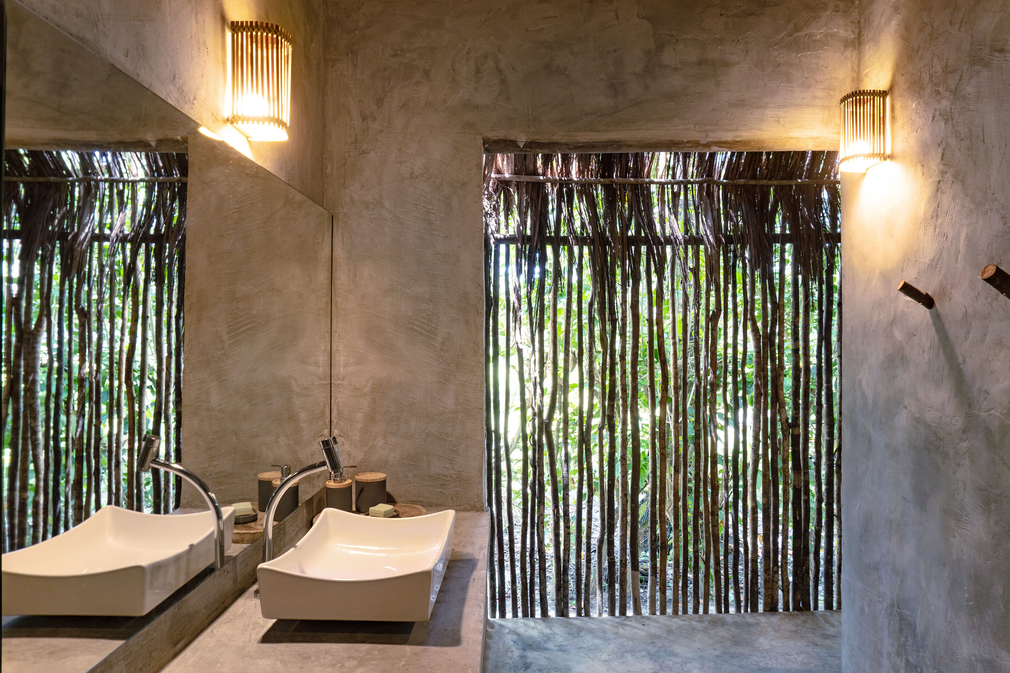 Un baño con dos lavamanos, un espejo y una ventana con persianas verticales.