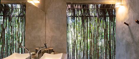 Un baño con dos lavamanos, un espejo y una ventana con persianas verticales.