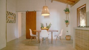 Een eetruimte met een houten tafel, witte stoelen, een hanglamp en potplanten.