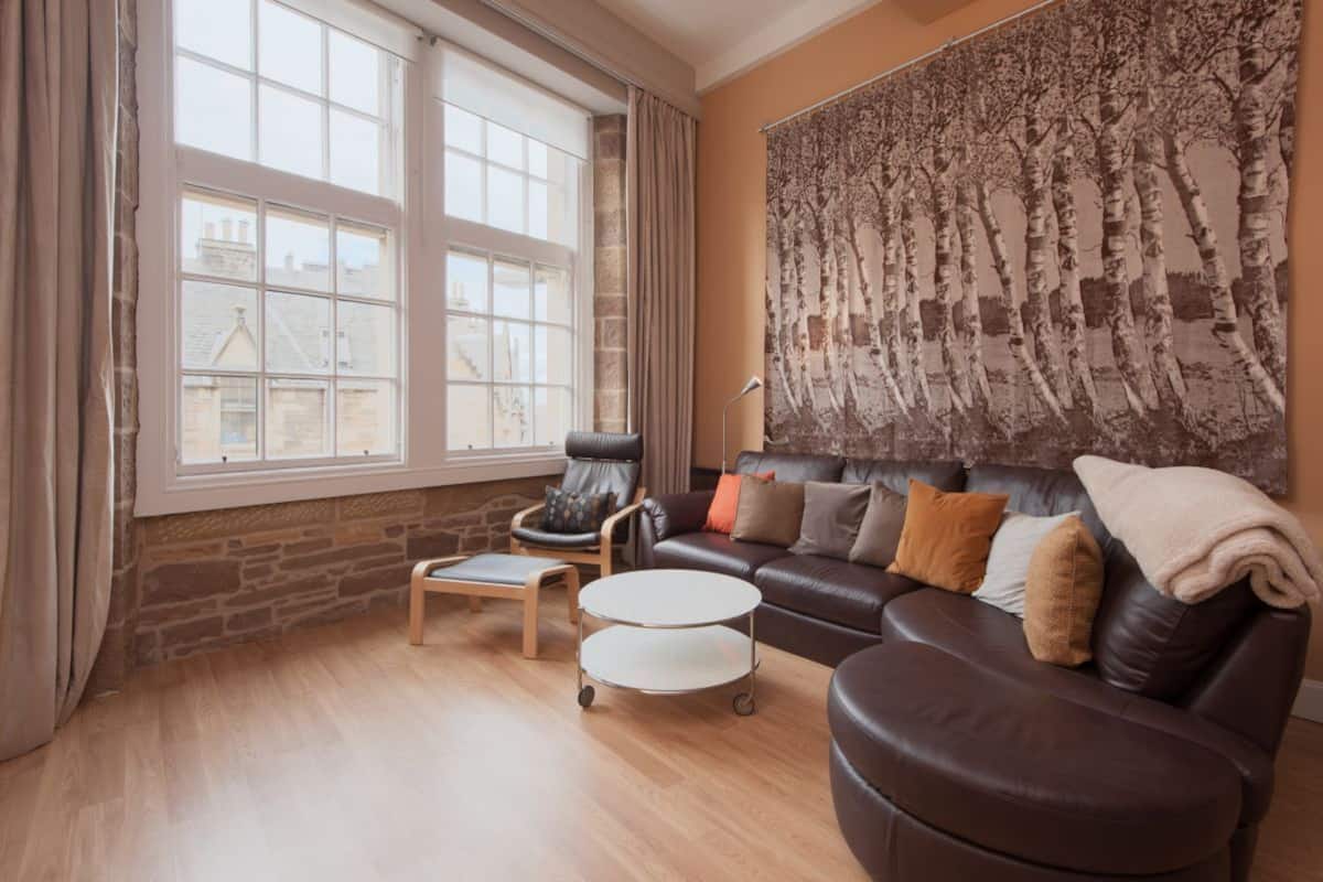 Ein Wohnzimmer mit einer Ledersofa, einem Holztisch, einem Sessel und einem großen Fenster.