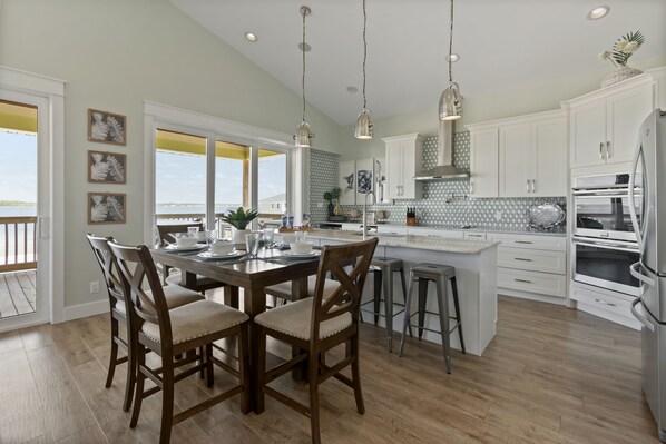 A spacious kitchen with a large island, white cabinetry, and pendant lighting. - Private home with sweeping water views, 2 min walk to the beach. Sleeps 13! (Navarre)