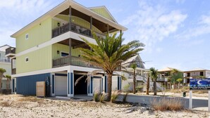 A multi-story beachfront property with a green and blue exterior, a balcony on the upper floor, and a sign for Sandy Beach Blessings. - Private home with sweeping water views, 2 min walk to the beach.  Sleeps 13! (Navarre)