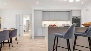 A modern kitchen with grey cabinets, a central island with bar stools, and a dining area with a wooden table and grey chairs. - Captivating 4-bed House in Killin (Killin)