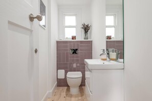 Un baño pequeño con un inodoro blanco, un lavamanos con espejo y una ventana sobre el lavamanos.