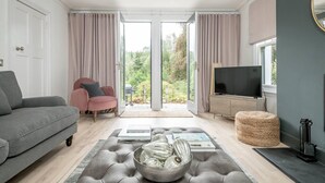 A modern living room with a grey sofa, a pink armchair, a TV, and a large window with curtains. - Captivating 4-bed House in Killin (Killin)