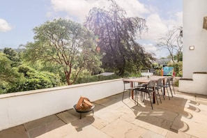Una terraza en la azotea con mesa y sillas, un hogar para fuego y vistas a árboles circundantes.