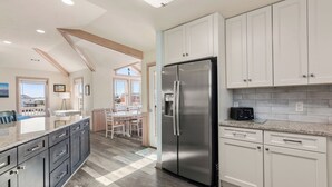 A modern kitchen with white cabinets, a stainless steel refrigerator, and a granite countertop. - O'Shinn View: Short Walk to Beach | Pool, Hot Tub (Corolla)