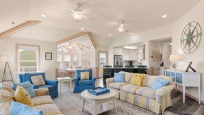 A spacious living room with multiple seating areas, a kitchen in the background, and a large window. - O'Shinn View: Short Walk to Beach | Pool, Hot Tub (Corolla)