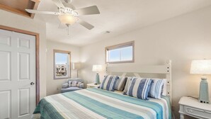 A bedroom with a bed, a ceiling fan, a window, and a nightstand with a lamp. - O'Shinn View: Short Walk to Beach | Pool, Hot Tub (Corolla)