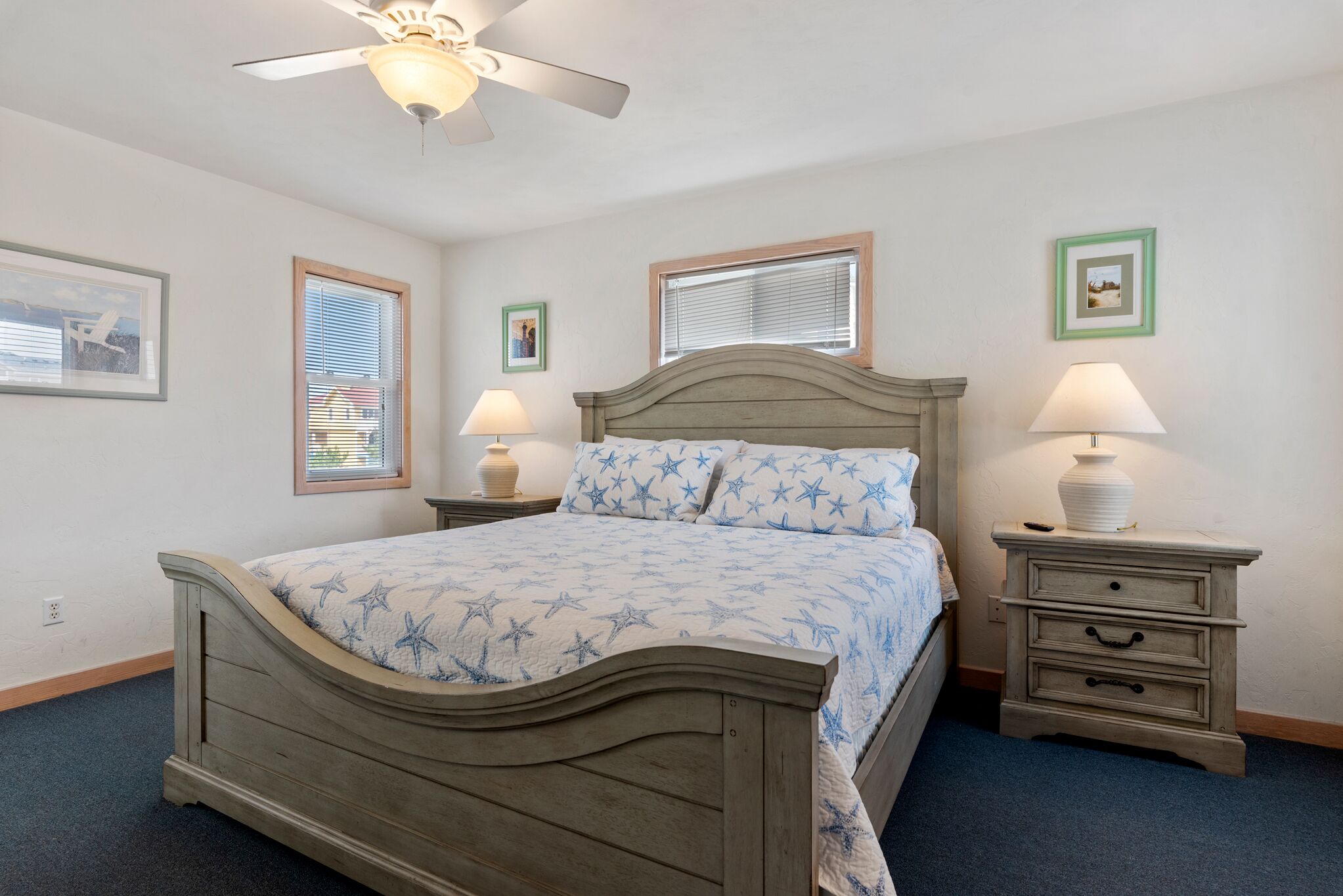 A bedroom with a bed, two bedside tables, a ceiling fan, and framed pictures on the walls.