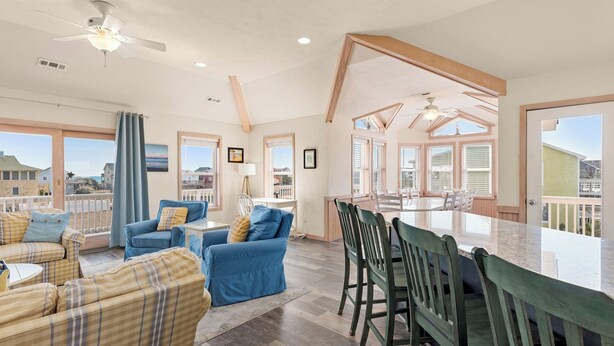 A spacious living area with a large dining table, multiple seating options, and a view of the surrounding landscape. - O'Shinn View: Short Walk to Beach | Pool, Hot Tub (Corolla)