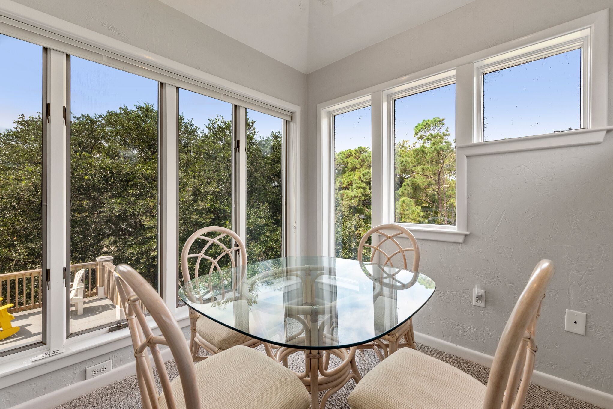 Une pièce d’angle avec une table en verre et quatre chaises, de grandes fenêtres et une vue sur les arbres.