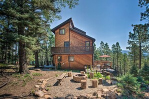 Une cabane en bois dotée d’un balcon, entourée d’arbres et comprenant un espace aménagé pour faire un feu de camp.