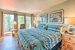 A spacious bedroom with a large bed, a chair, a nightstand, and a window with curtains.