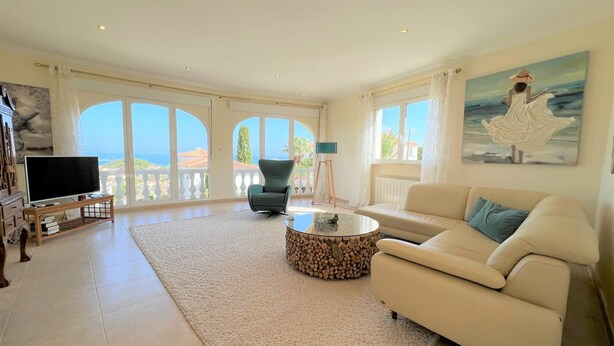 A spacious living room with a large TV, comfortable seating, a fireplace, and a view of the sea.