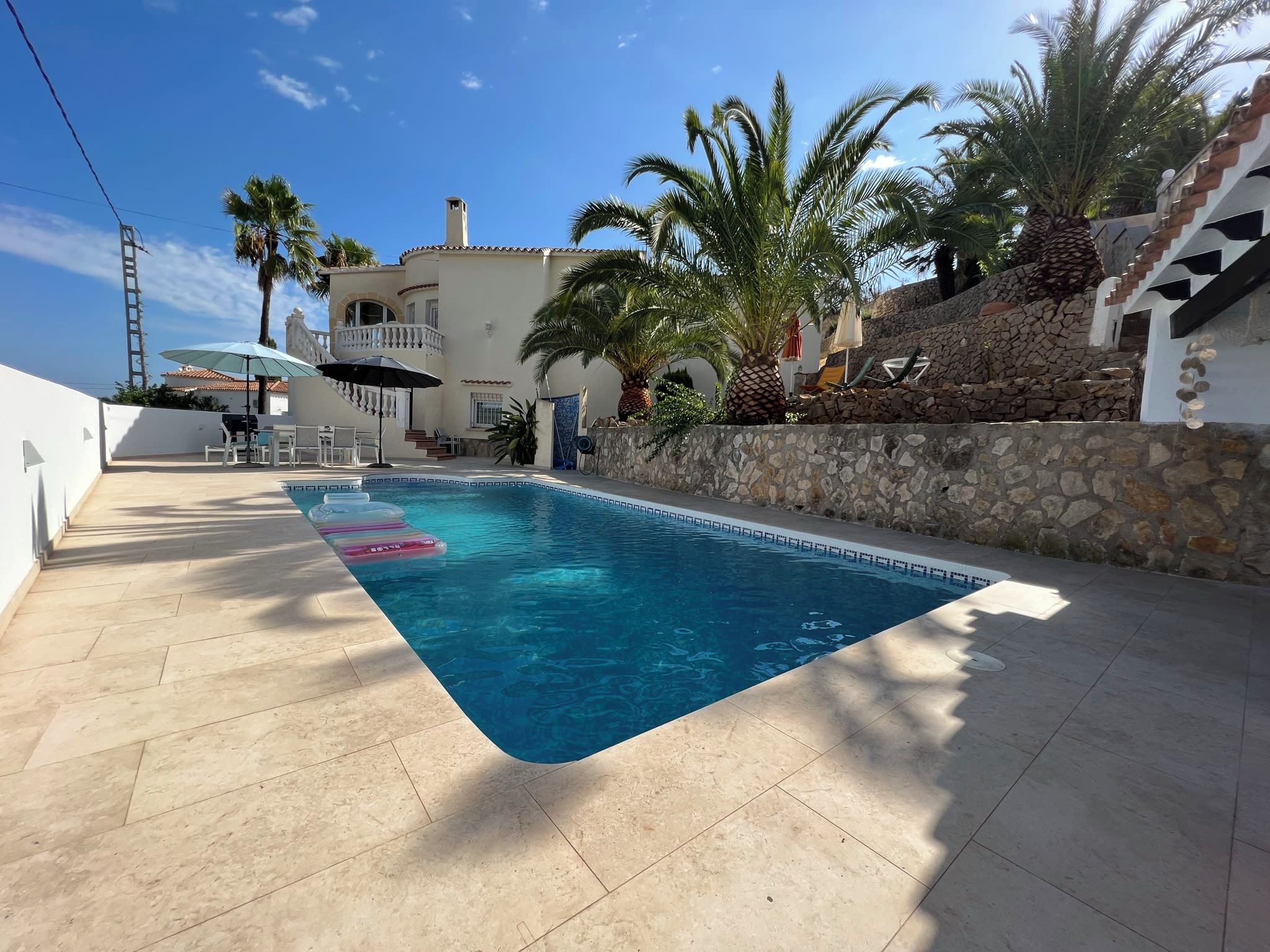 A swimming pool with a stone wall and palm trees.