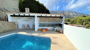A poolside area with a seating area, stone walls, and a view of mountains.