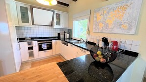A modern kitchen with white cabinets, a black countertop, and a built-in oven. There is a window with a view of greenery outside.