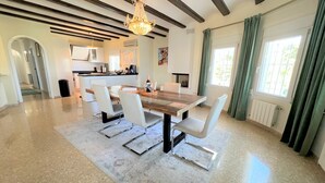 A modern kitchen with white cabinets, a wooden island, and a dining area with a large table and white chairs.