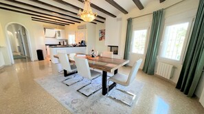 Una cocina moderna con comedor, que incluye una mesa de madera, sillas blancas y una araña.