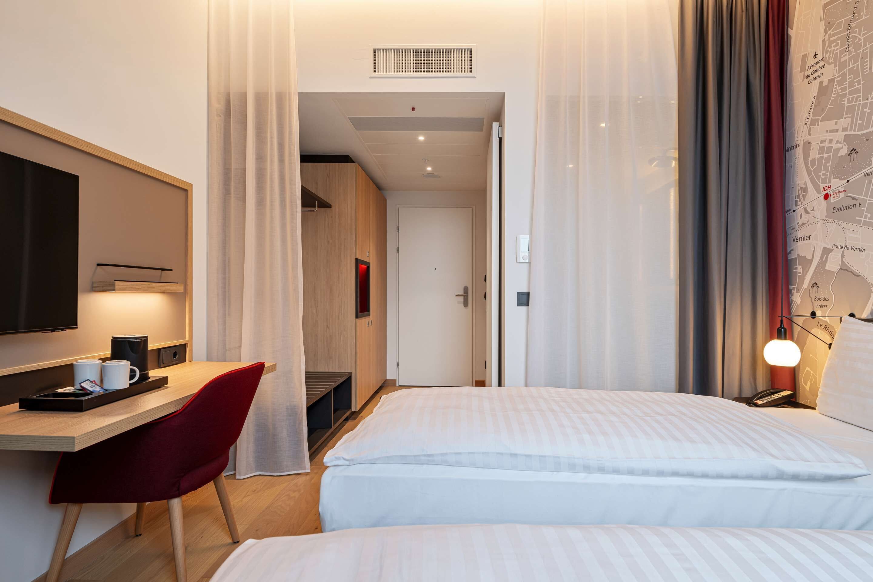 A hotel room with a bed, a desk with a chair, a TV, and a map on the wall.