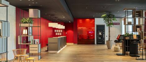 A modern lobby with wooden flooring, red walls, and a reception desk.