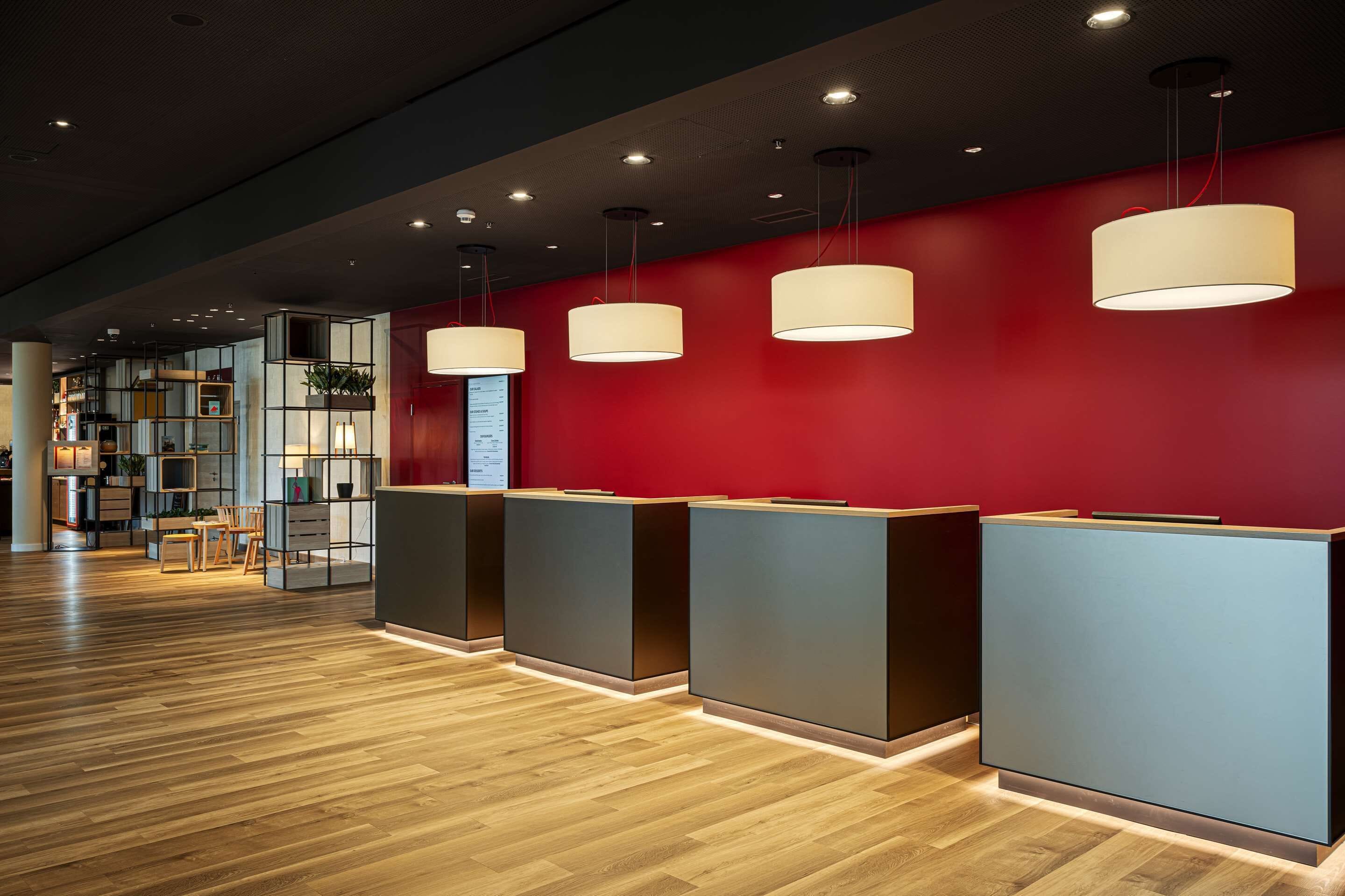 A reception area with a red wall, wooden flooring, and modern pendant lighting.