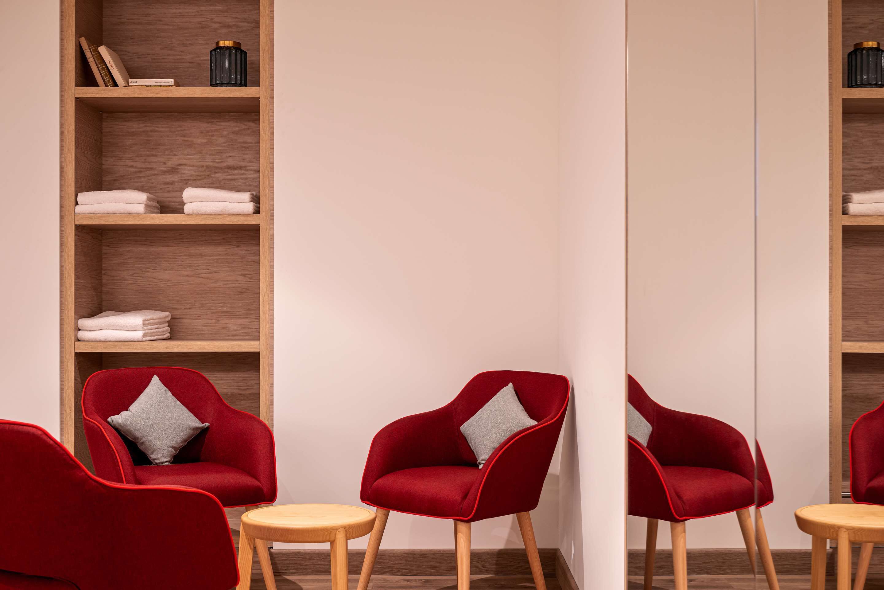A modern room with two red armchairs, a wooden floor, and a bookshelf with folded towels.