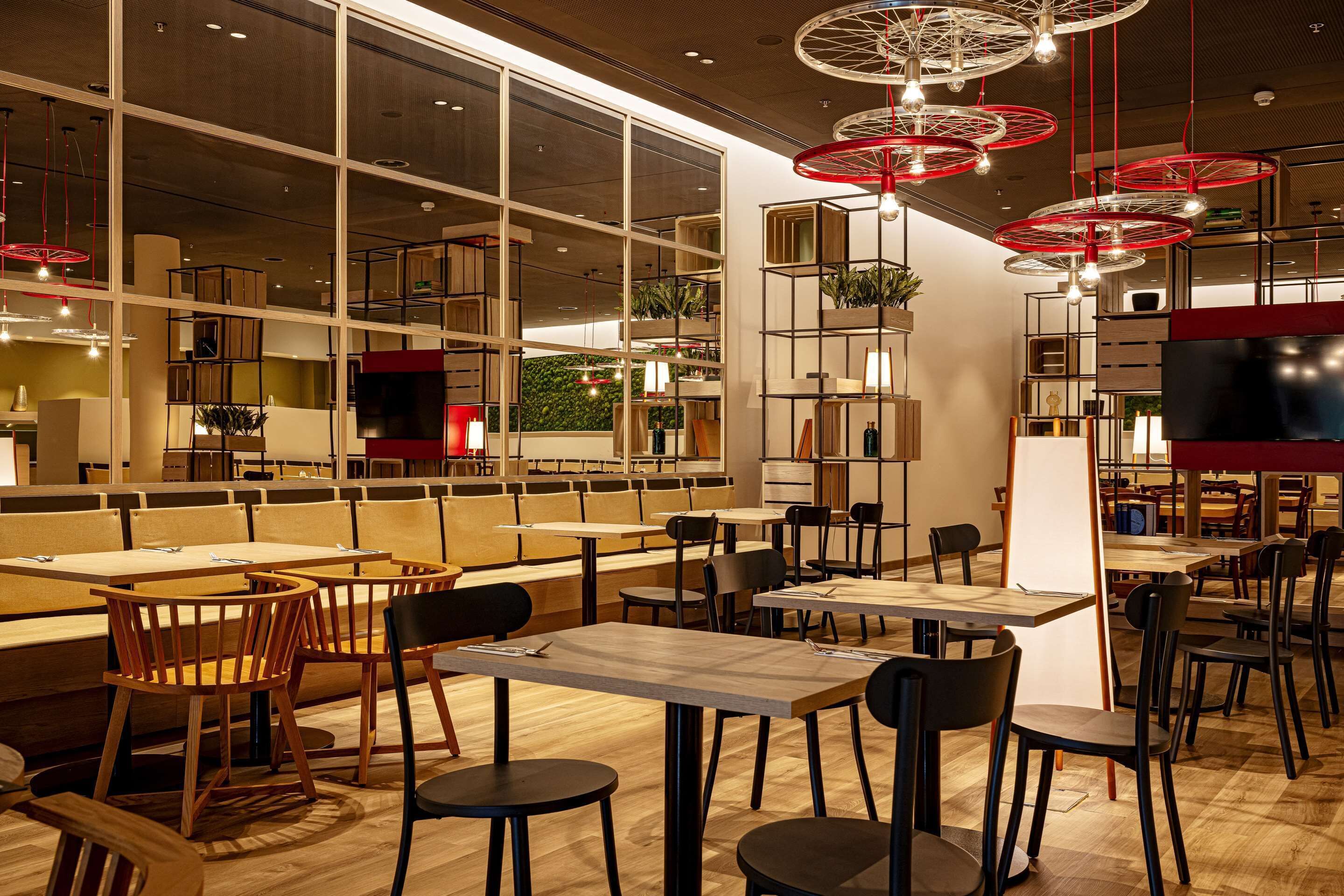 A modern restaurant with high ceilings, wooden furniture, and red circular light fixtures.