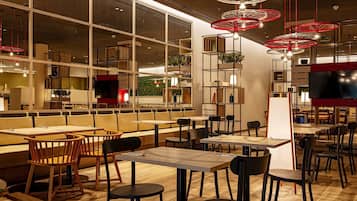 A modern restaurant with high ceilings, wooden furniture, and red circular light fixtures.