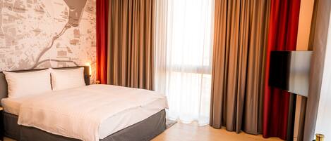 A hotel room with a bed, a map wall, a TV, and a red chair.