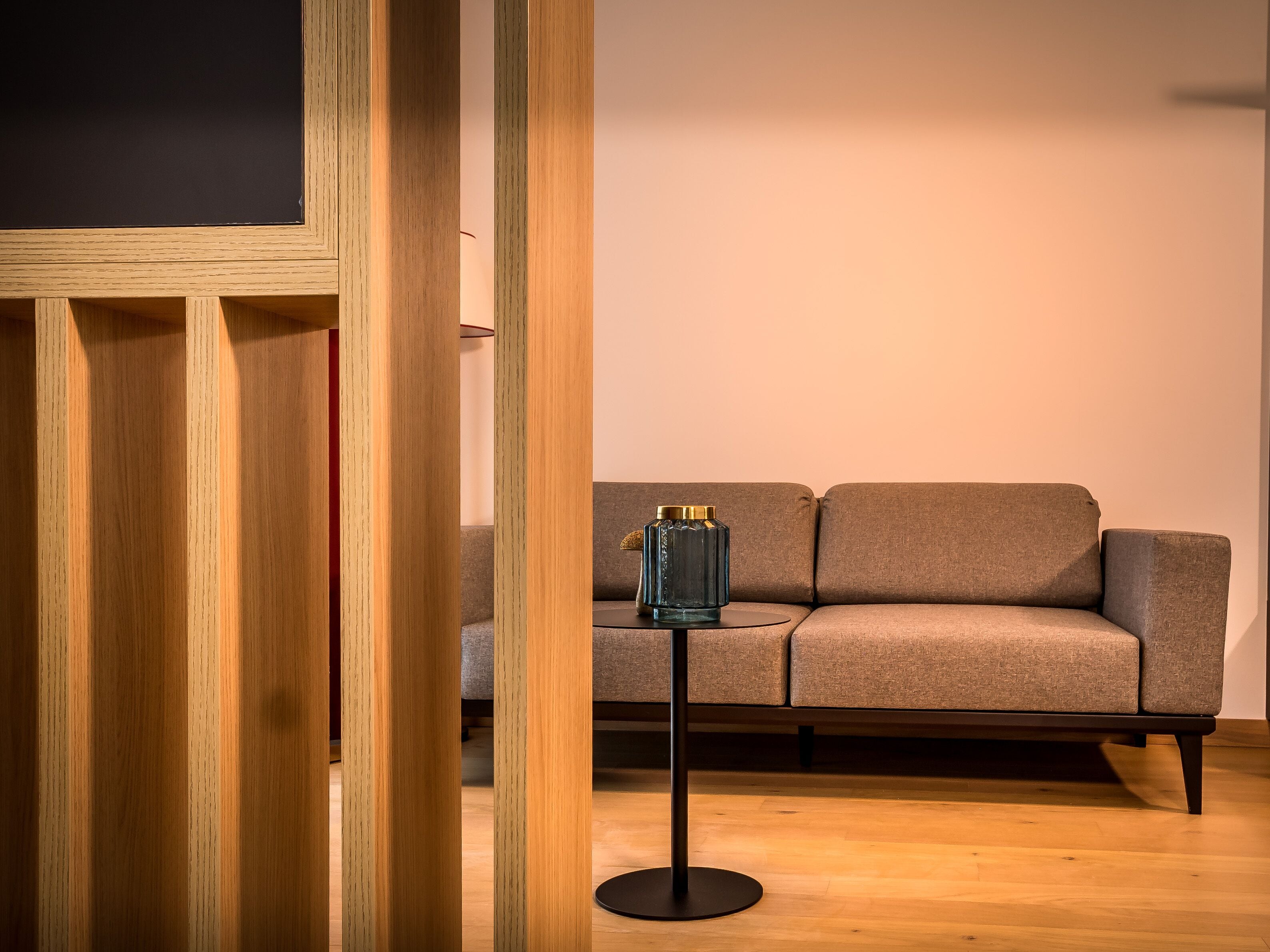 Un salon moderne avec un plancher en bois, un canapé gris et une table en verre agrémentée d’un objet décoratif.