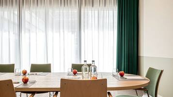 A conference room with a wooden table, green chairs, and a large window with sheer curtains.