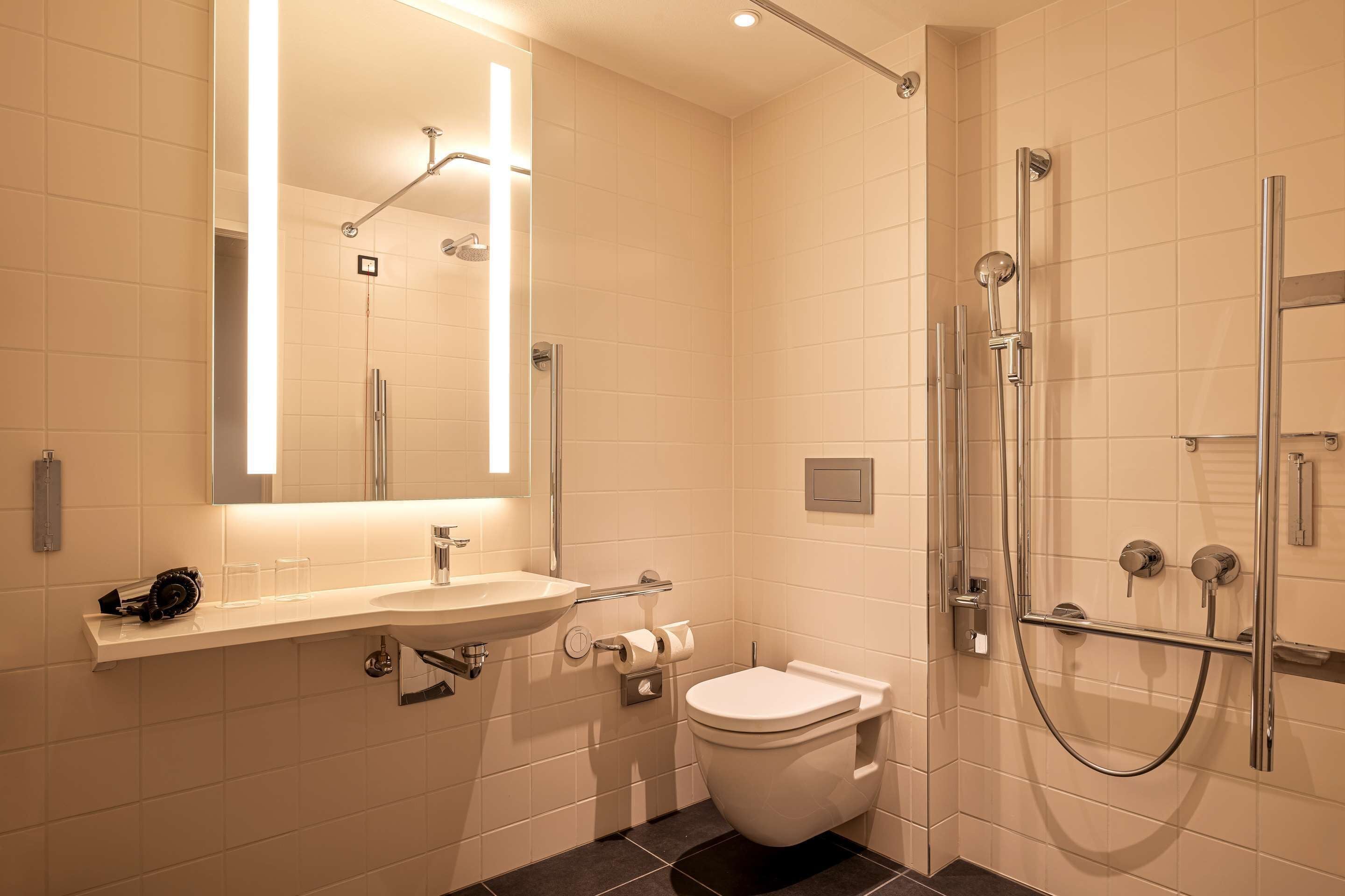 Un bagno moderno con lavandino, specchio e water bianchi, dotato di un soffione manuale e cabina doccia in vetro.