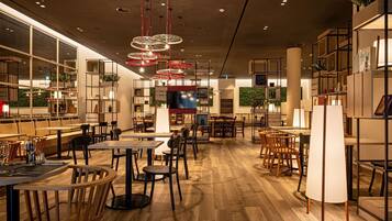 Ein geräumiges Restaurant mit Holztischen und -stühlen, roten Hängeleuchten und einem großen Fernseher.