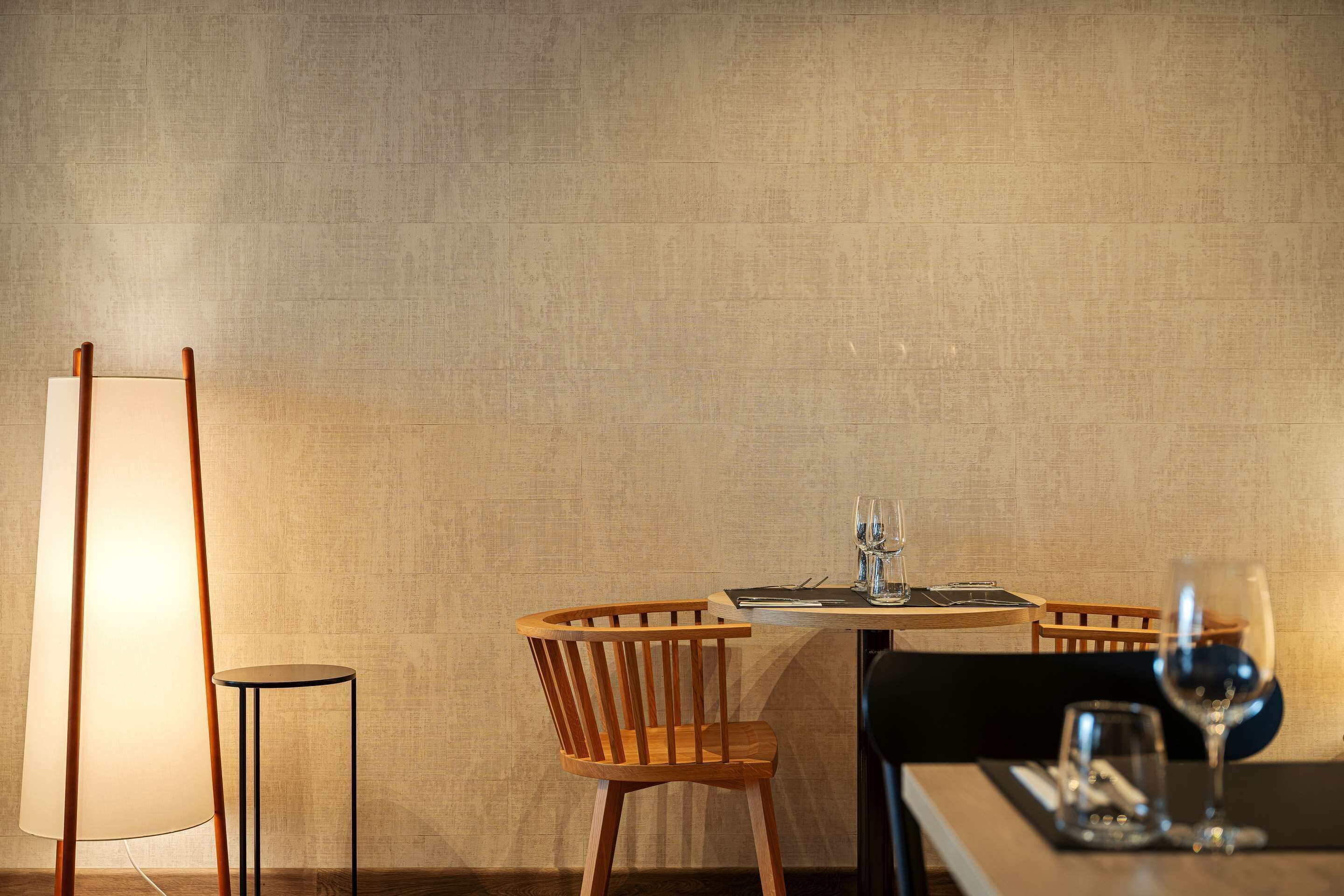 Un coin repas avec une table dressée pour deux personnes, une chaise en bois, un lampadaire et un verre à vin.