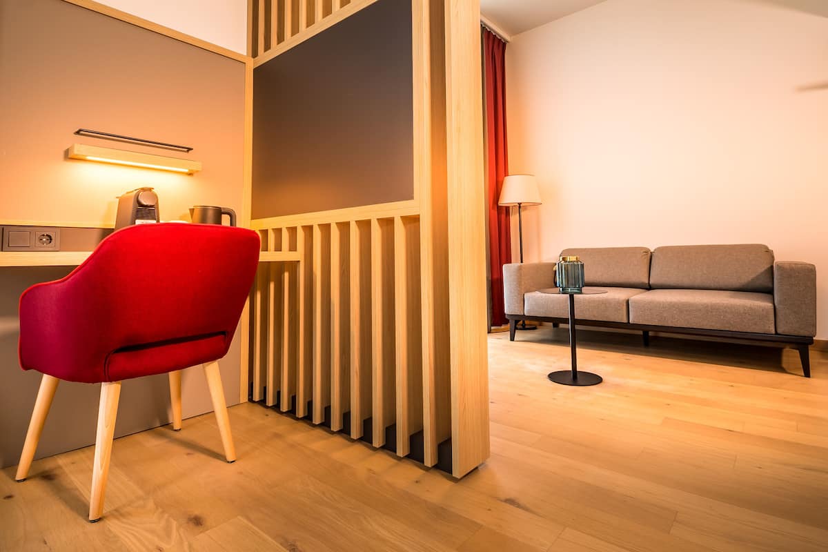 Une pièce moderne avec un séparateur en bois, un fauteuil rouge, un canapé gris et une lampe.