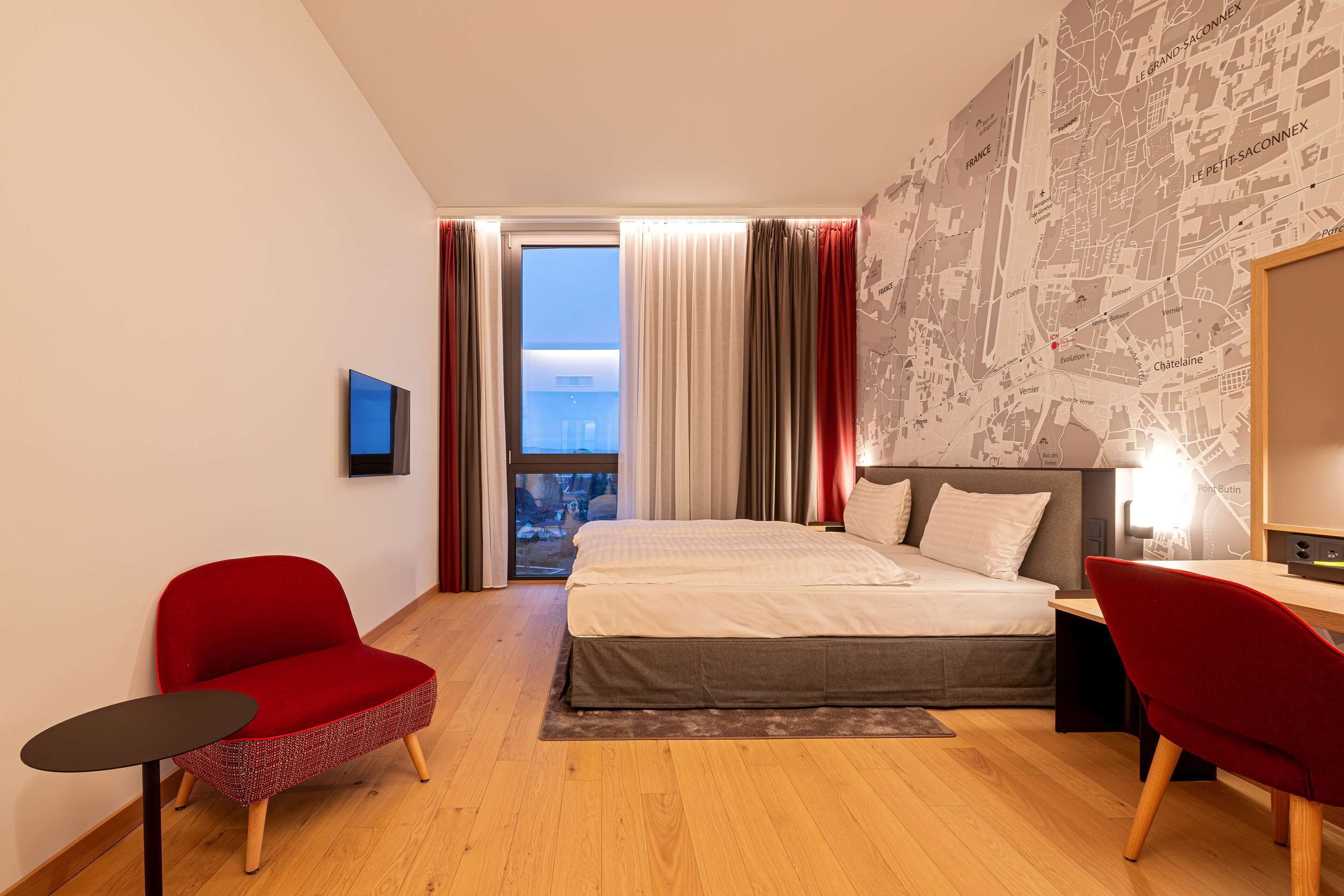 A modern hotel room with a large bed, a desk, a chair, and a view of the city through the window.