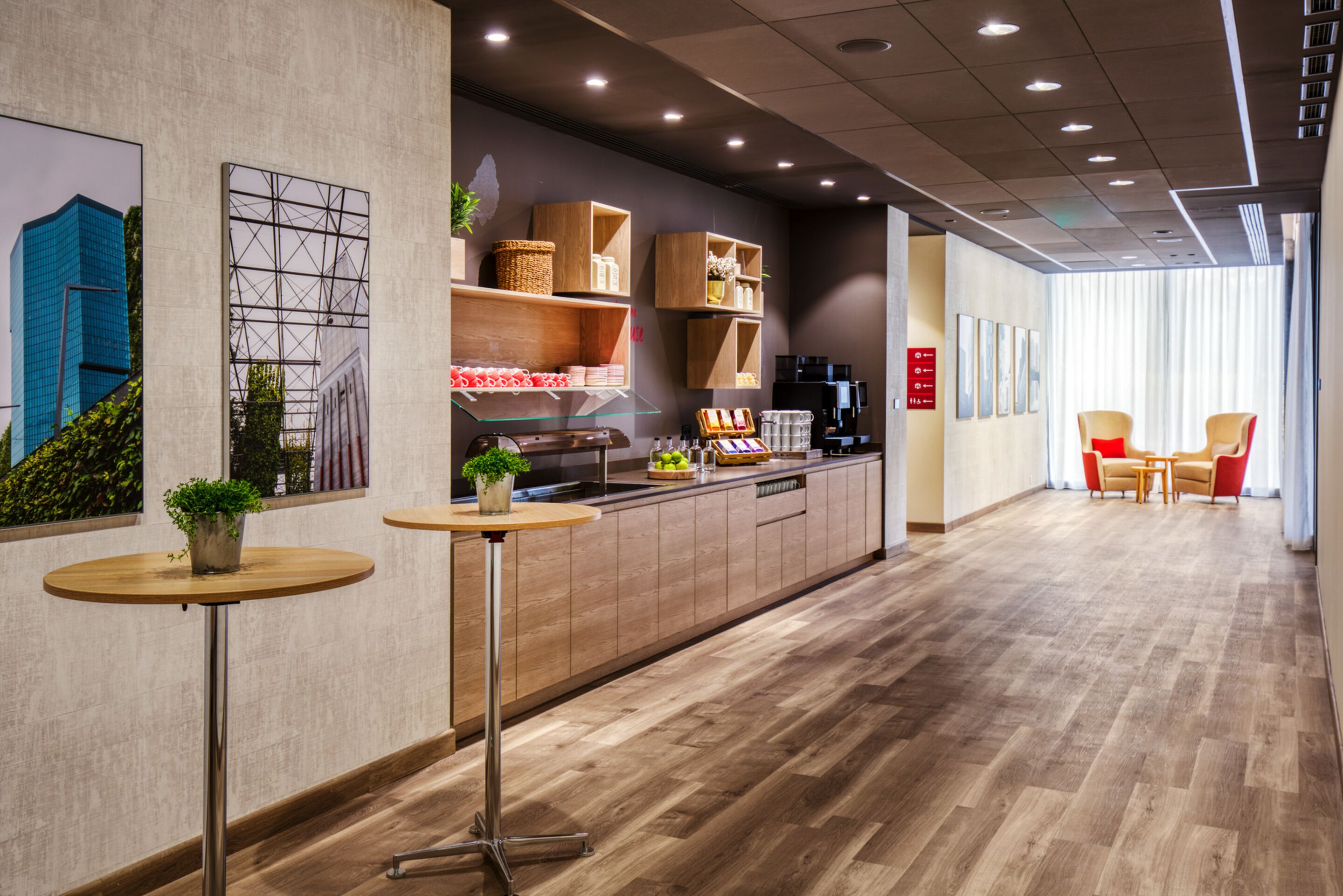 A modern interior with a wooden floor, a kitchen area with a coffee machine, and a seating area with chairs.
