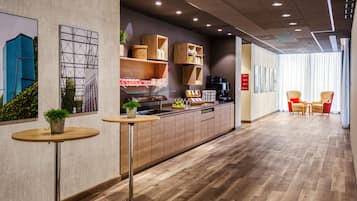 A modern interior with a wooden floor, a kitchen area with a coffee machine, and a seating area with chairs.