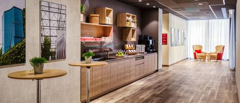 Et moderne interiør med trægulv, et køkkenområde med kaffemaskine og et siddeområde med stole.