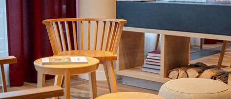 Una habitación moderna con muebles de madera, incluyendo una silla, un reposapiés y una estantería con libros y leña.