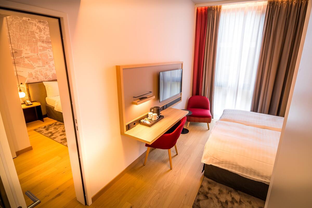 Une chambre d’hôtel avec un lit, un bureau avec une télévision, une chaise rouge et une carte accrochée au mur.