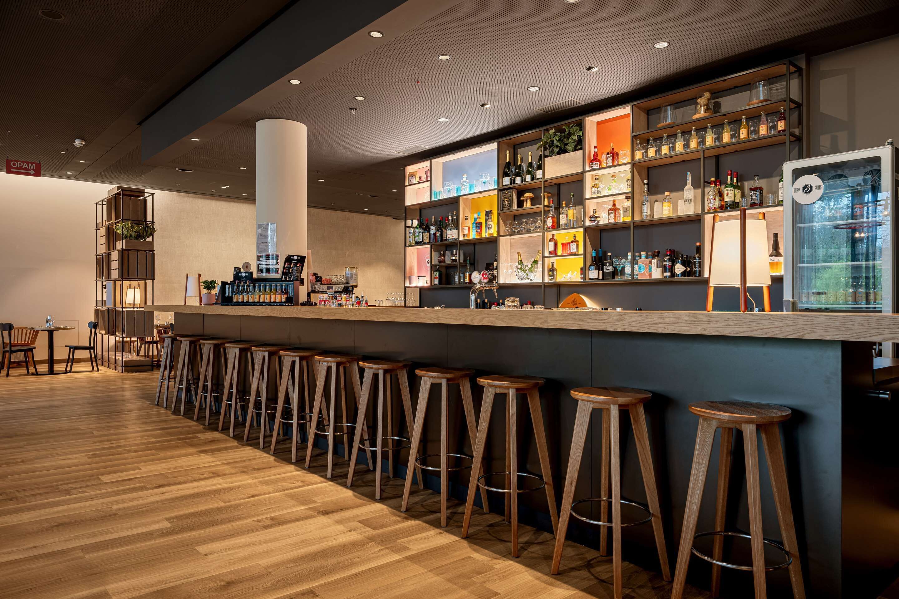 A bar area with wooden stools, a counter with various bottles, and a coffee machine.